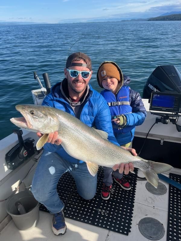 Man and child on a boat hold up a large fish, smiling. Blue water and sky in the background.