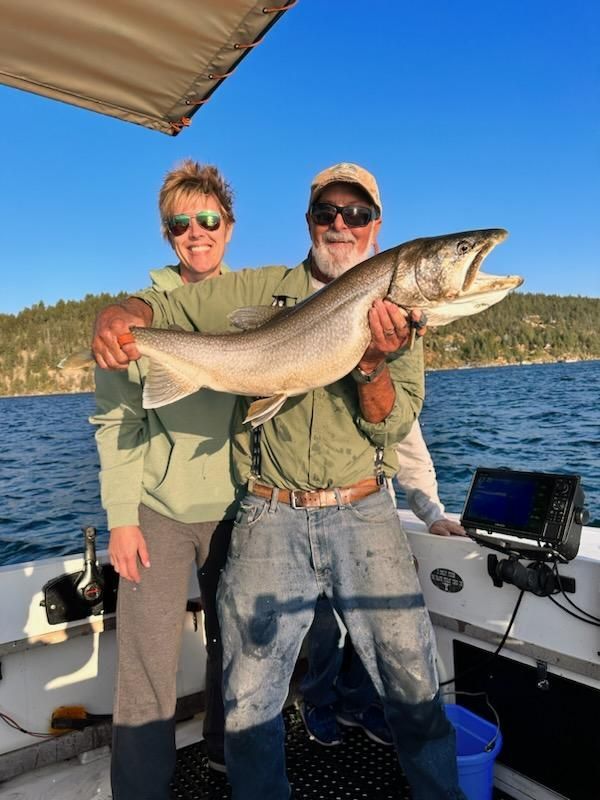 Man holding large fish with a woman; they are on a boat on a lake.