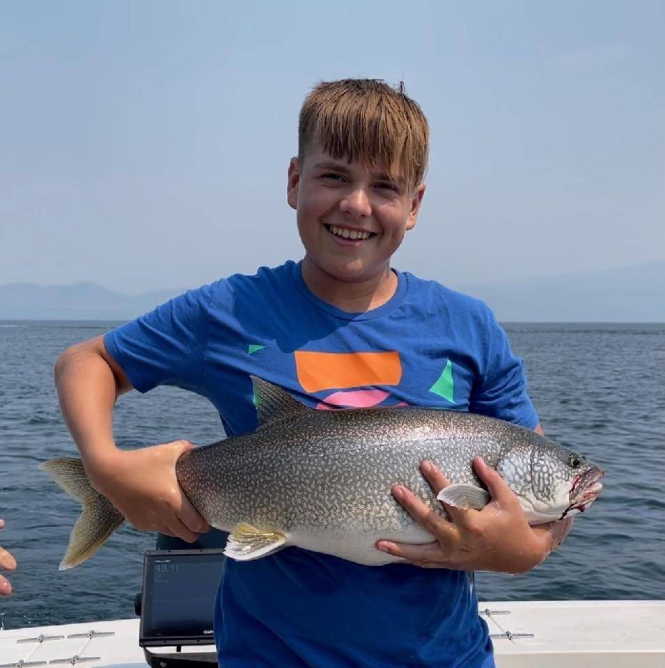 A young boy in a blue shirt is holding a large fish in his hands