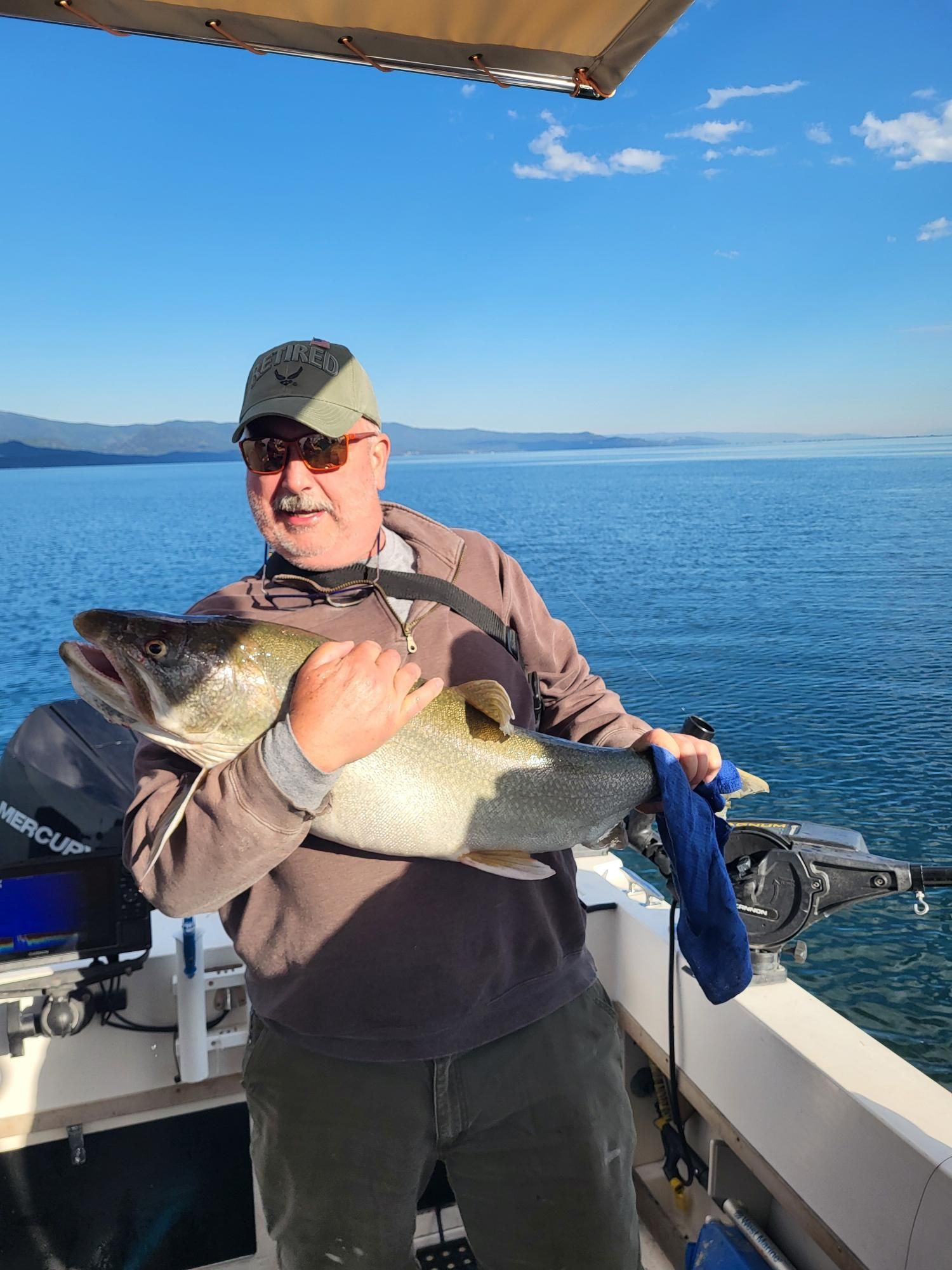 Man on boat holding a large fish, blue water, sunny day.
