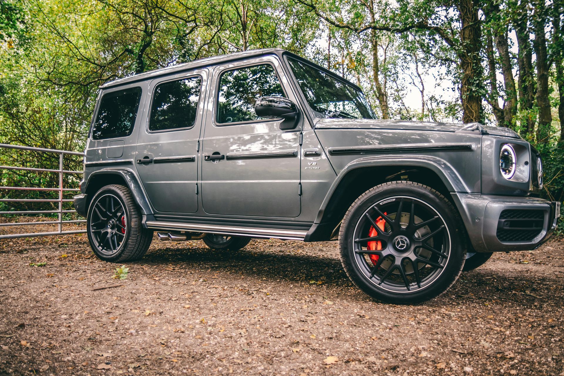 A mercedes benz g63 amg is parked in a dirt lot in the woods.