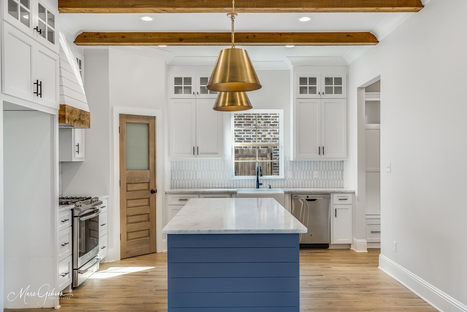 White kitchen with blue island, brass pendant lights, and wooden beams.