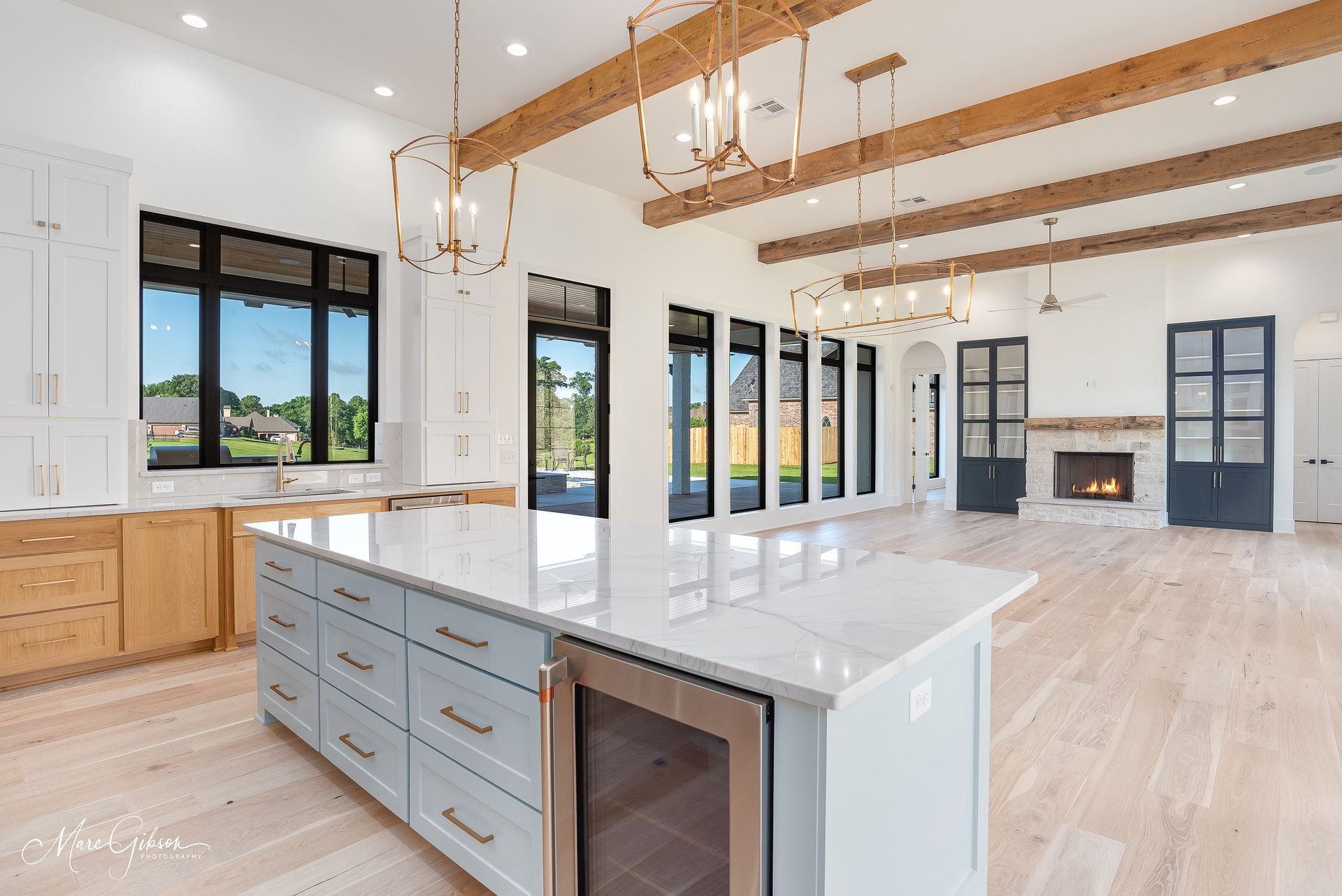 Open-concept kitchen with light wood floors, blue island, and exposed wooden beams.