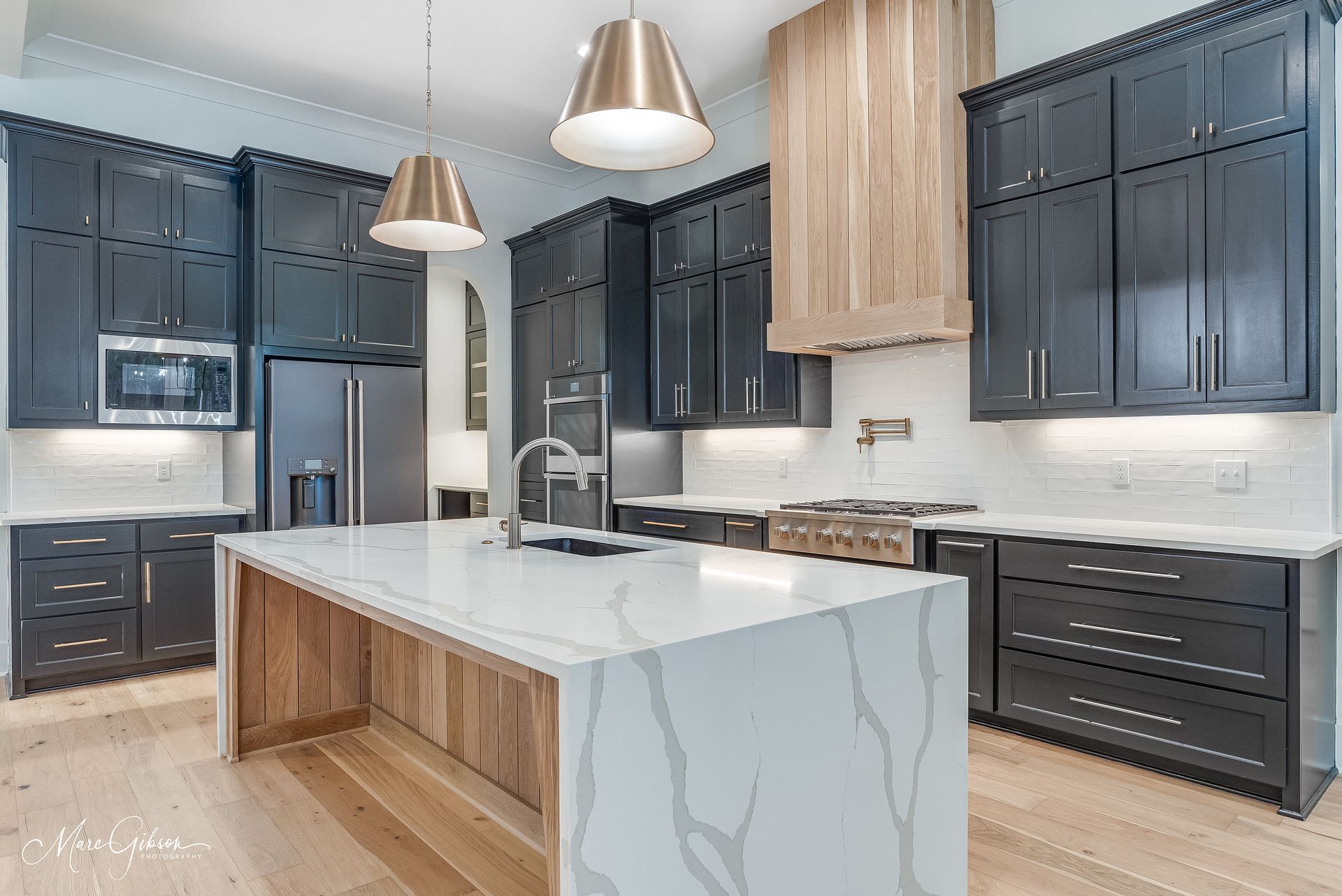 Modern kitchen with dark cabinets, white countertops, and a wood-paneled island.