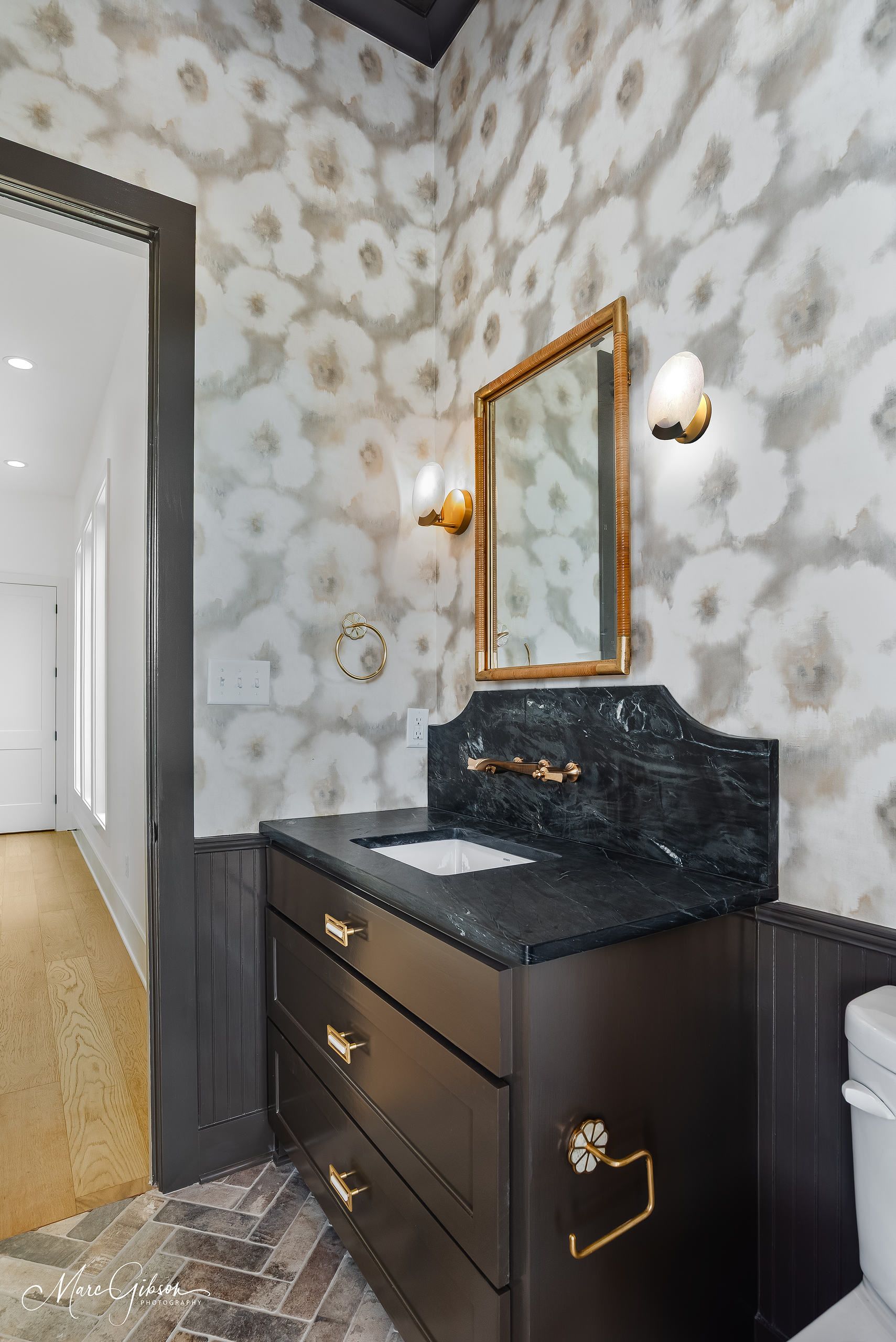 Powder room: Floral wallpaper, black vanity with gold fixtures, and a marble countertop.