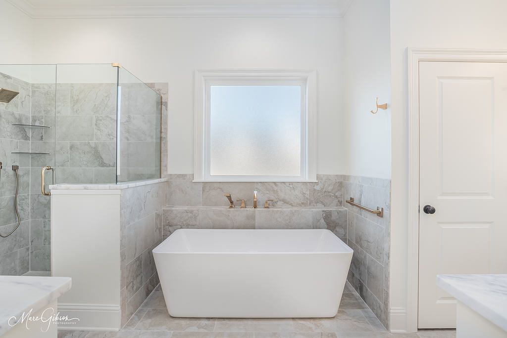 Modern bathroom with white tub, frosted window, and glass shower.