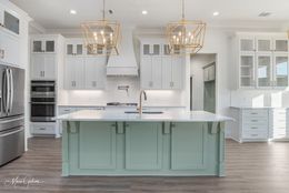 Modern kitchen with white cabinets, sage green island, and gold light fixtures.