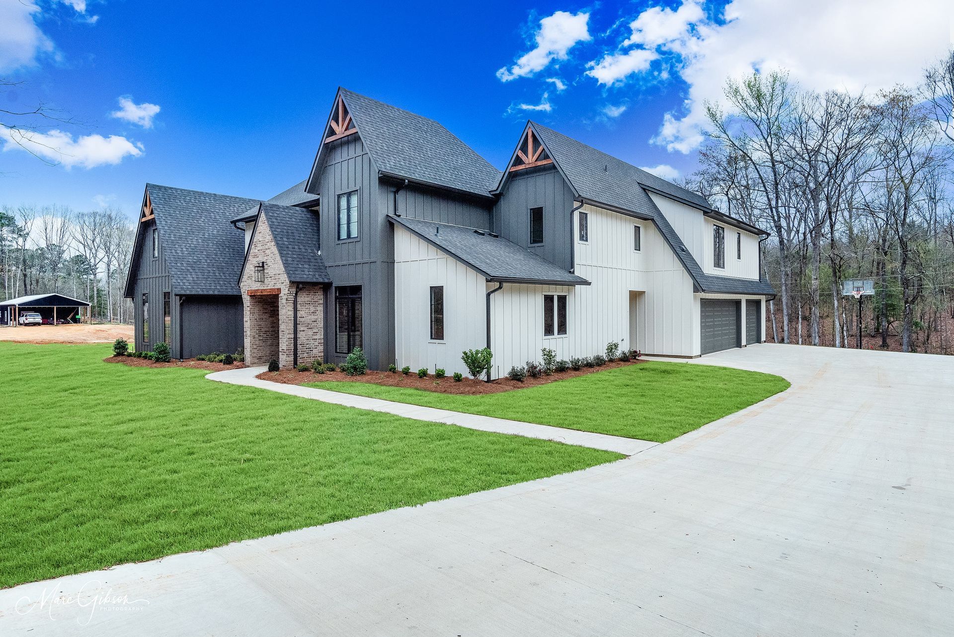 Modern two-story home with gray and white siding, dark roof, brick accents, and a large green lawn.
