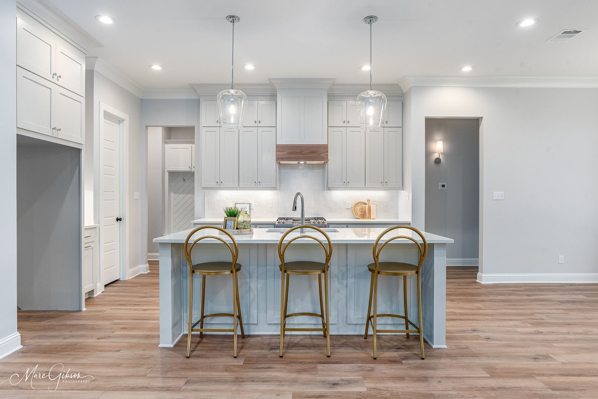 Modern kitchen with white cabinets, island with gold stools, and wooden floors.