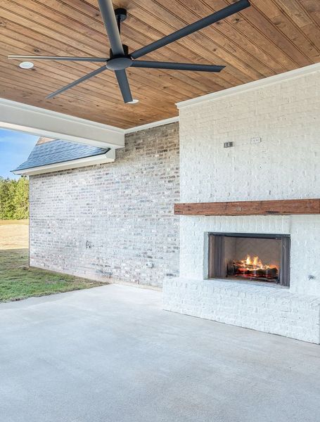 Outdoor patio with white brick fireplace, wood ceiling, and large ceiling fan.