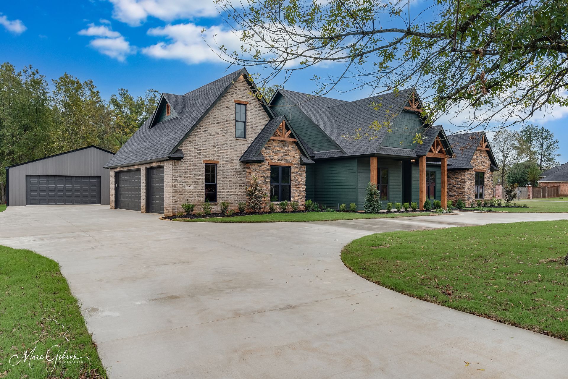 A large brick home with a green door, attached garage, and circular driveway on a grassy lawn.