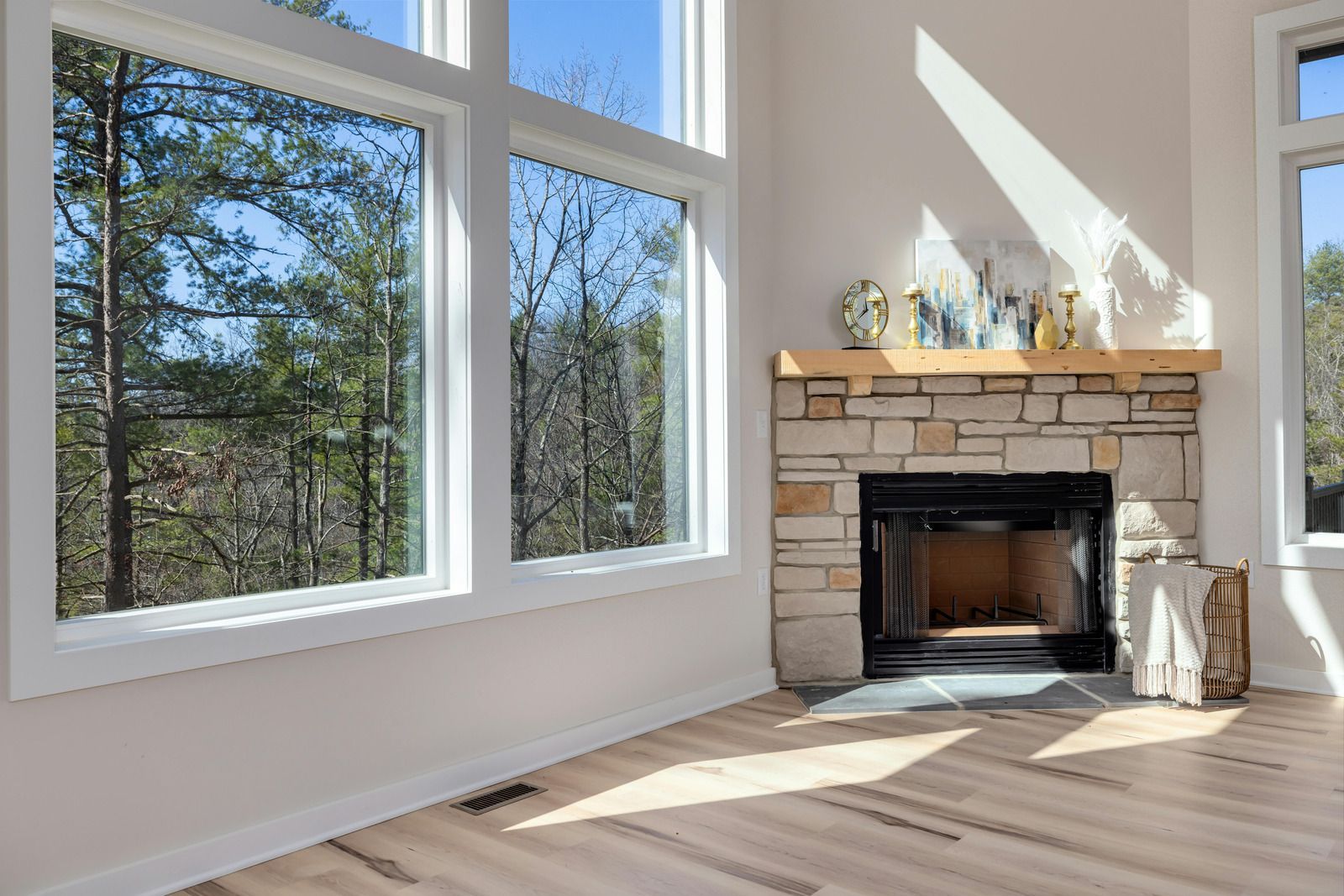 Sunlit living room with large windows and a stone fireplace on a light wood floor