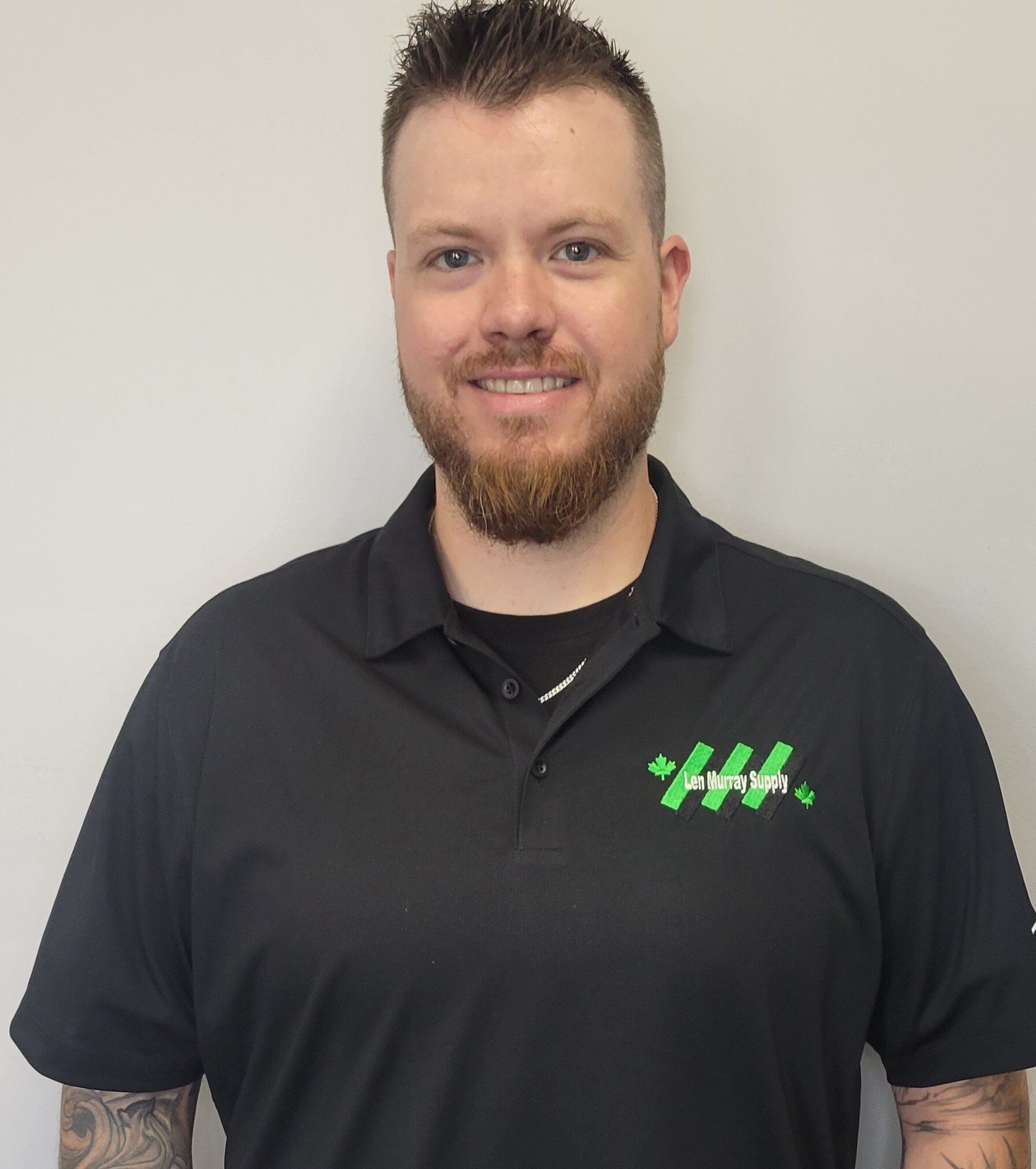 Un homme avec une barbe porte une chemise noire avec un logo vert dessus.