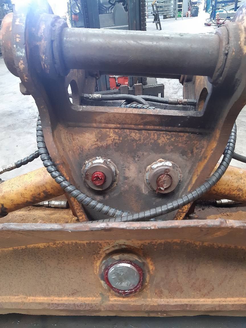 Close-up of a rusted metal machine part with bolts and a central pin in an industrial setting
