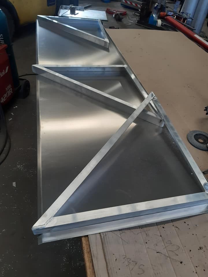 Metal wedge-shaped frame with silver panels and diagonal braces on a workbench