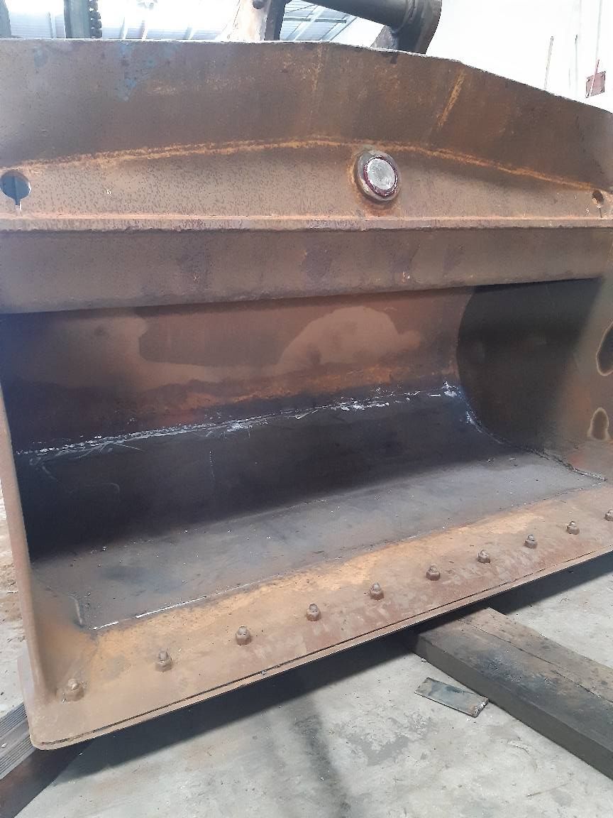 Rusty metal machine hopper with a dark interior and bolt-lined base