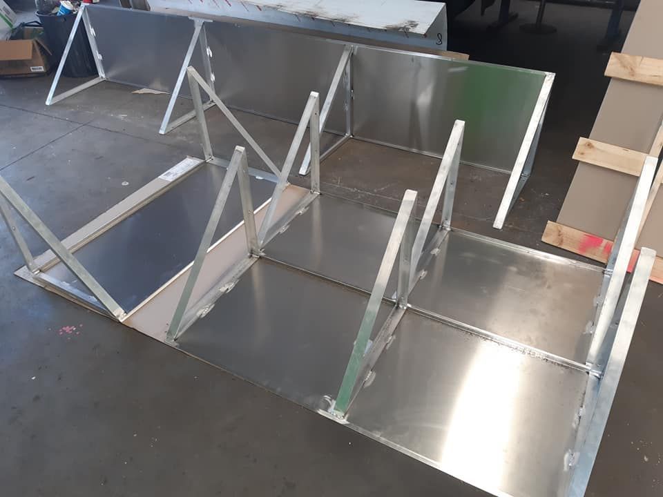 Metal frames and panels arranged on a warehouse floor, showing several silver triangular and rectangular structures.