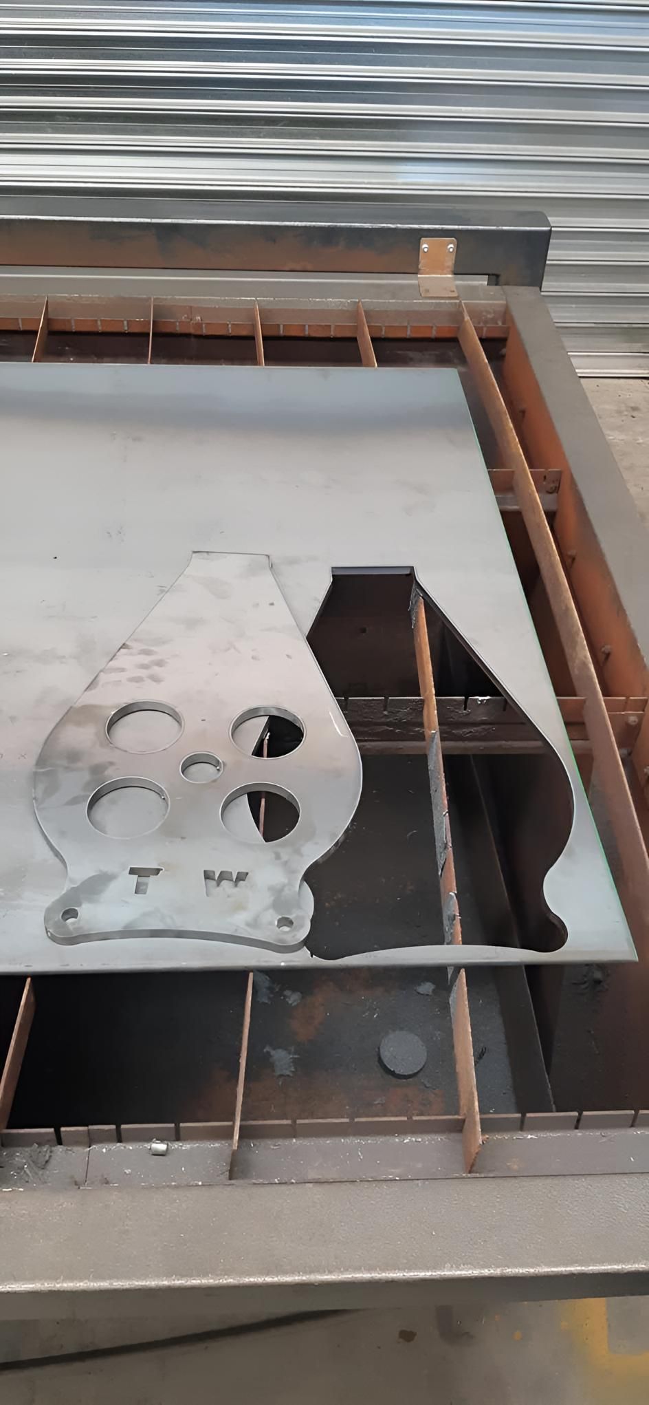 Metal cutout plate and rusted beams over a grated opening with water below