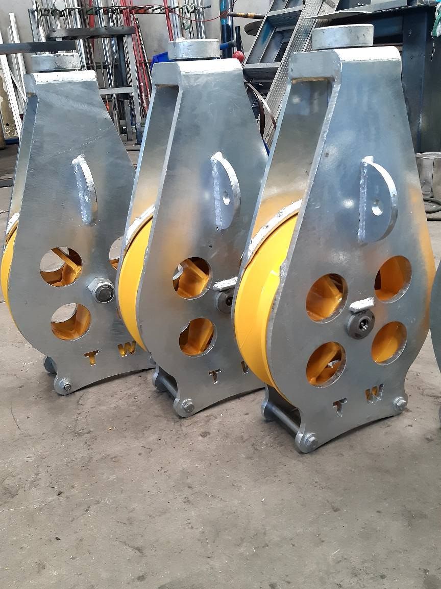 Three silver metal parts with yellow circular cutouts standing on a workshop floor