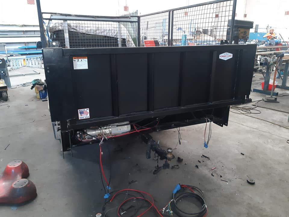 Black truck bed/dump trailer with wiring and hoses in a workshop garage.