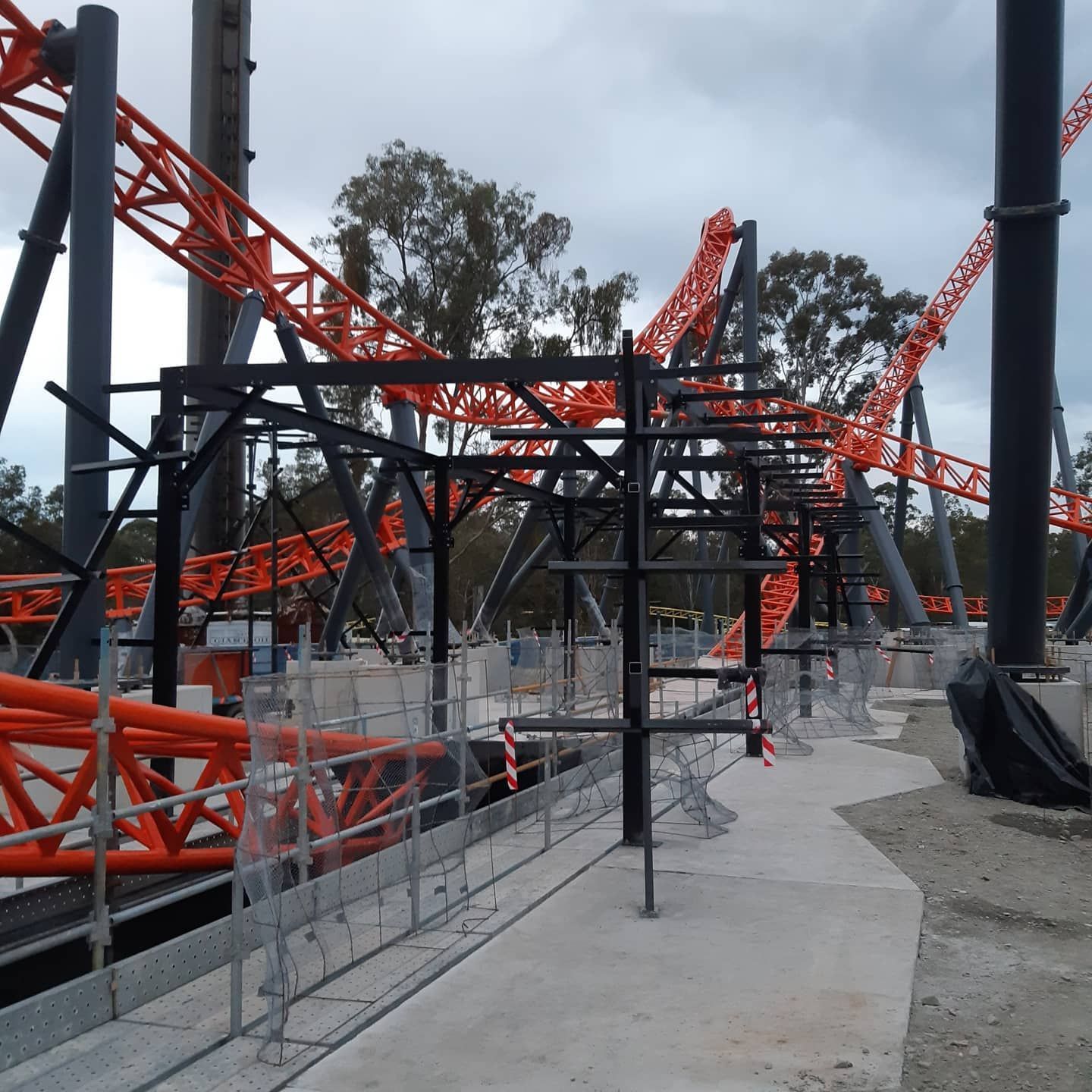 Orange roller coaster tracks under construction with steel supports and concrete walkways