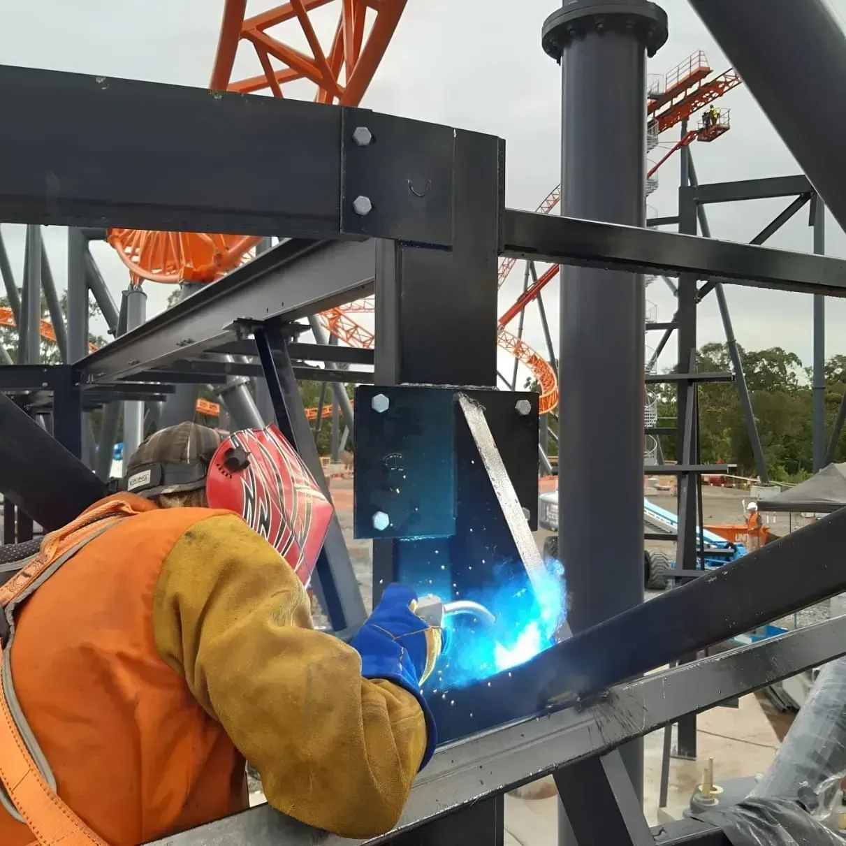 Worker welding a black steel frame with bright blue sparks at an industrial site