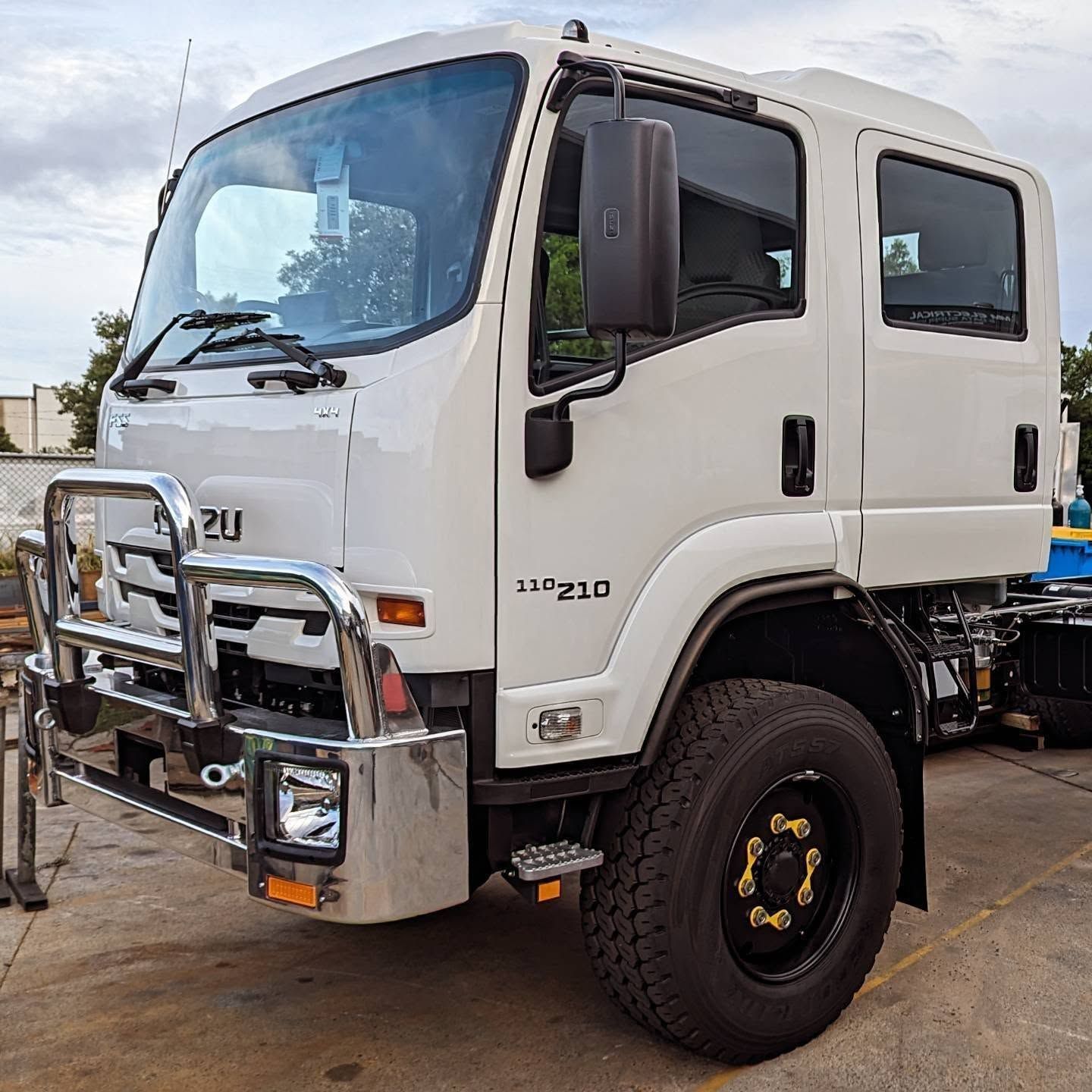 White Isuzu cab-over truck with chrome bull bar, parked outdoors on a cloudy day