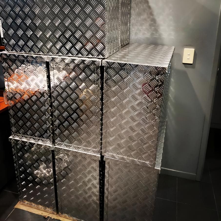 Stacked silver diamond-plate metal boxes in an indoor corner beside a wall switch.