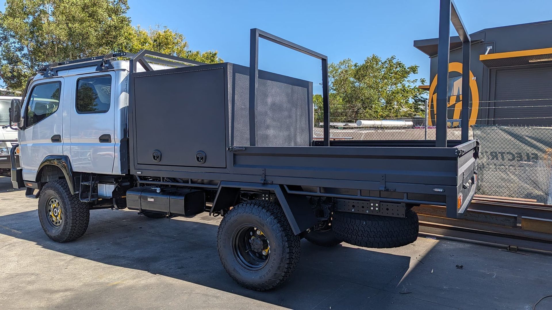 White flatbed truck parked outdoors, carrying a black metal gate panel on the bed.
