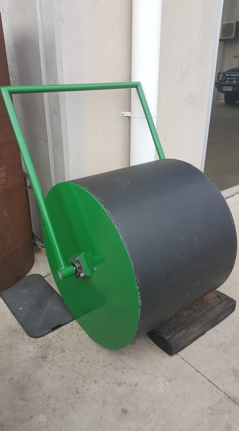 Green cart with a large black drum on concrete, leaning against a wall indoors.