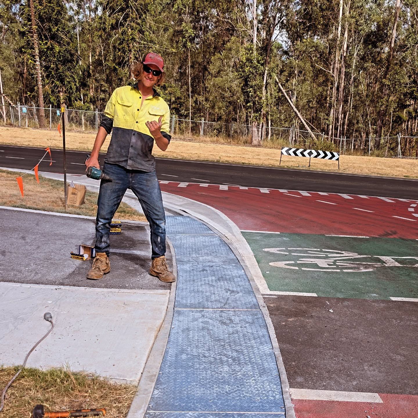 Worker in yellow shirt and boots stands beside a curb on a paved roadway