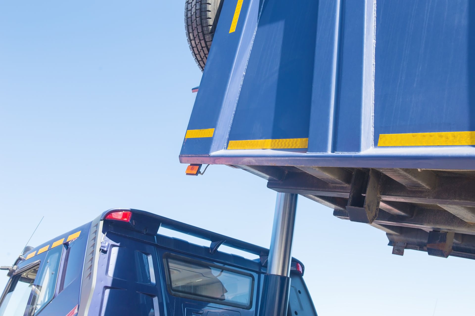Blue truck cab under a raised dump bed against a clear sky