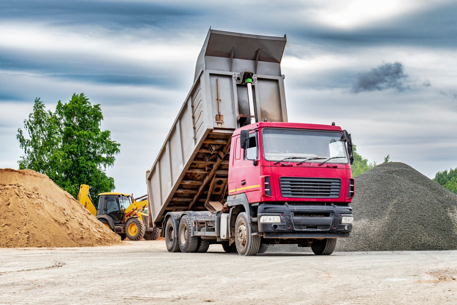 Pink dump truck unloading gravel at a construction site with sand piles and a loader