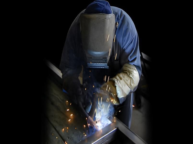 Welding worker in blue protective gear, sparks flying in a dark workshop.