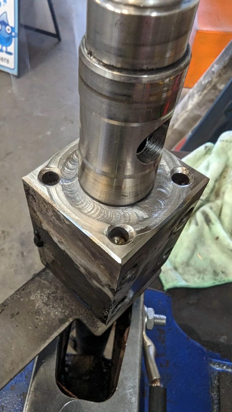 Metal press ram aligned over a square steel block in a workshop setup