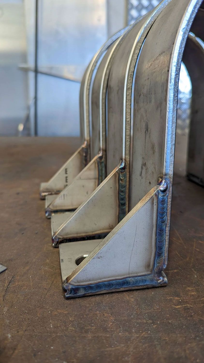 Row of silver metal brackets on a workbench, viewed from the side.