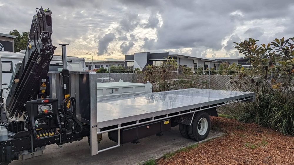 Flatbed truck with a crane carrying a large white plastic tank in a cloudy outdoor setting