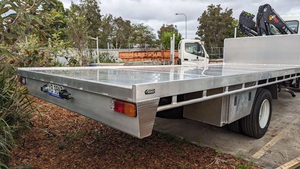 Silver flatbed truck parked outdoors, viewed from the rear-left side with a white cab.