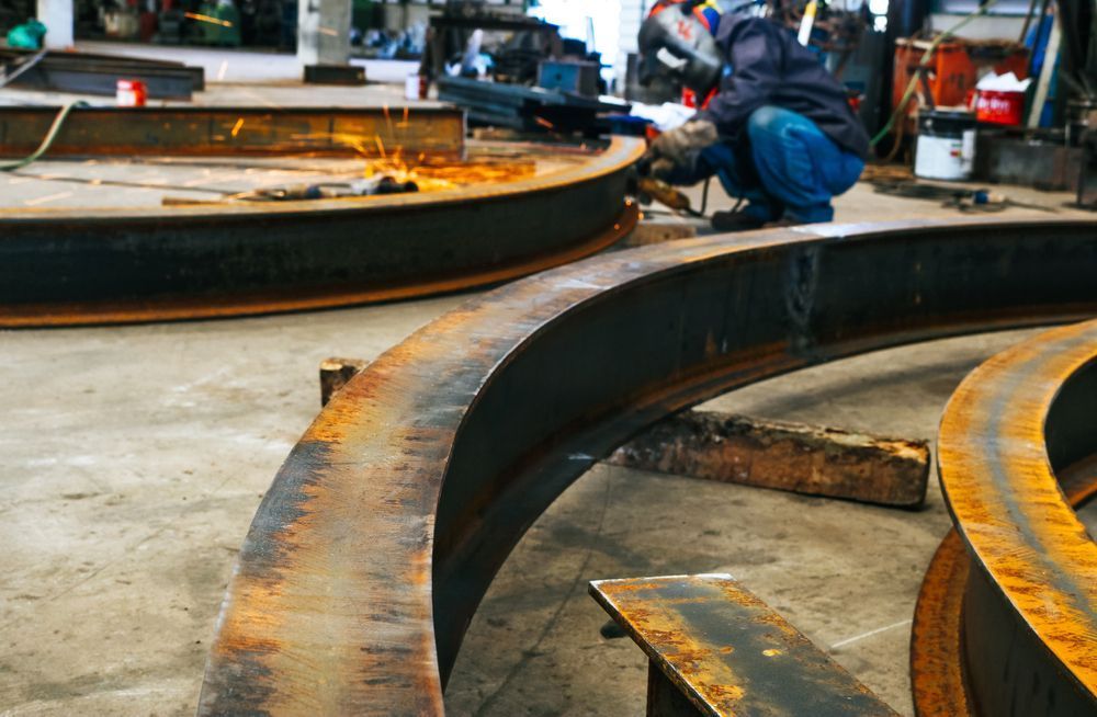 Workshop scene with large curved metal rings and a worker welding in the background