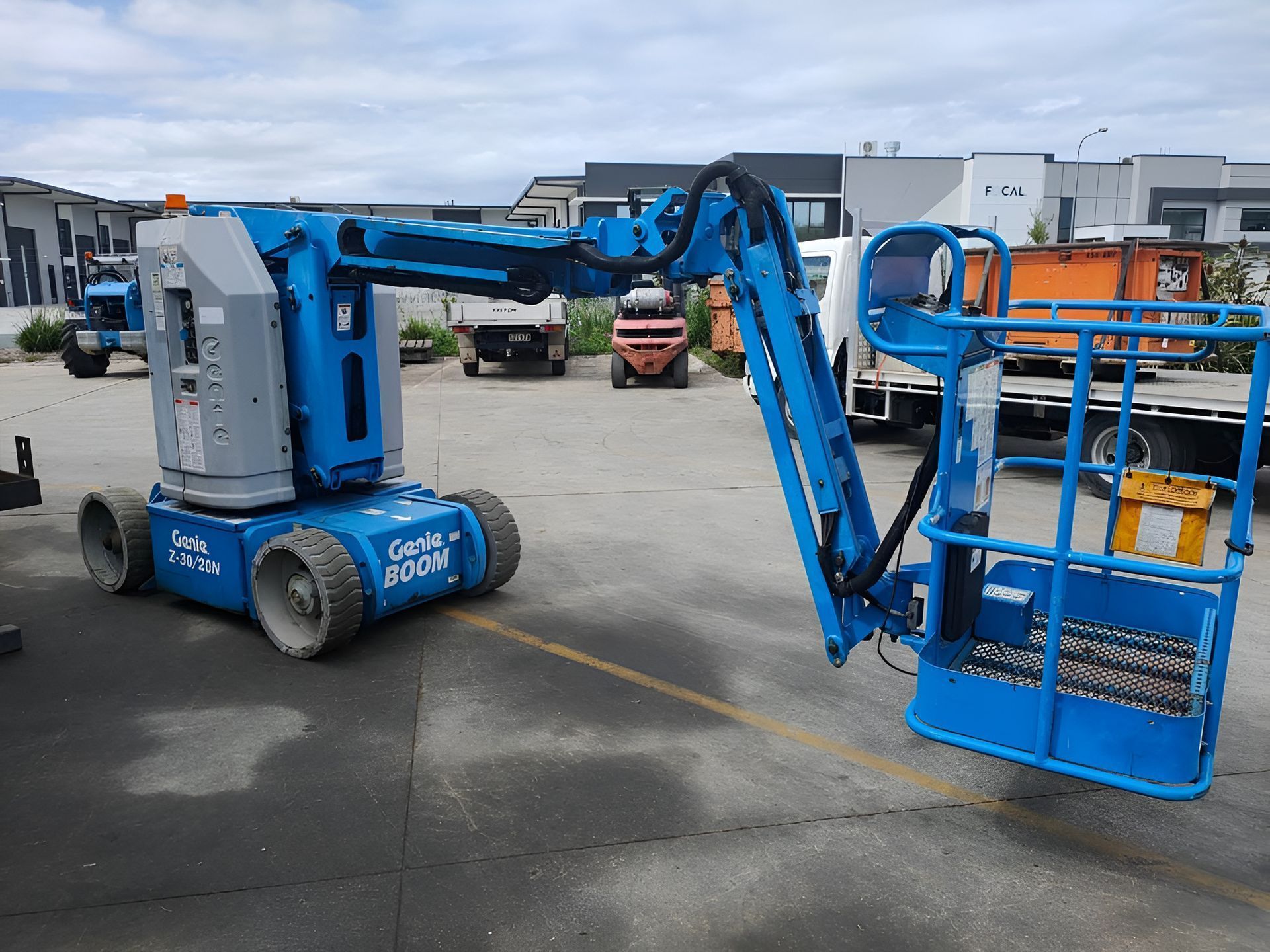 Blue boom lift extending to an orange work platform in an industrial yard.