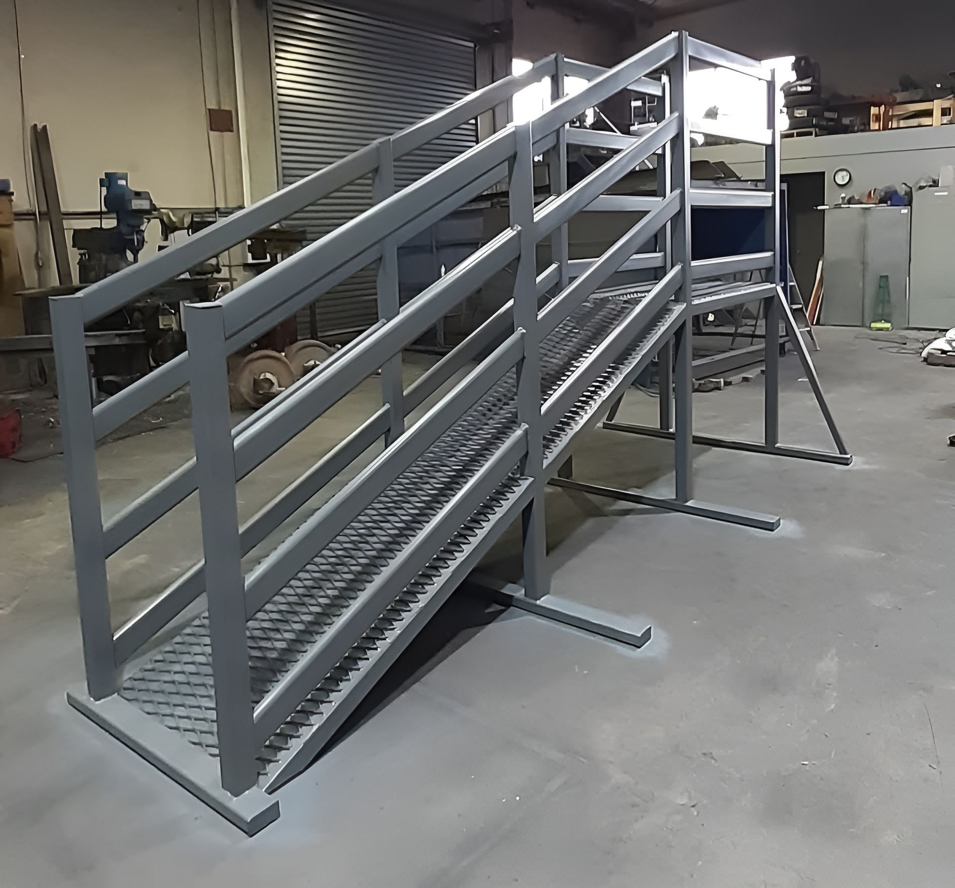 Gray metal wheelchair ramp with guardrails in an industrial warehouse setting