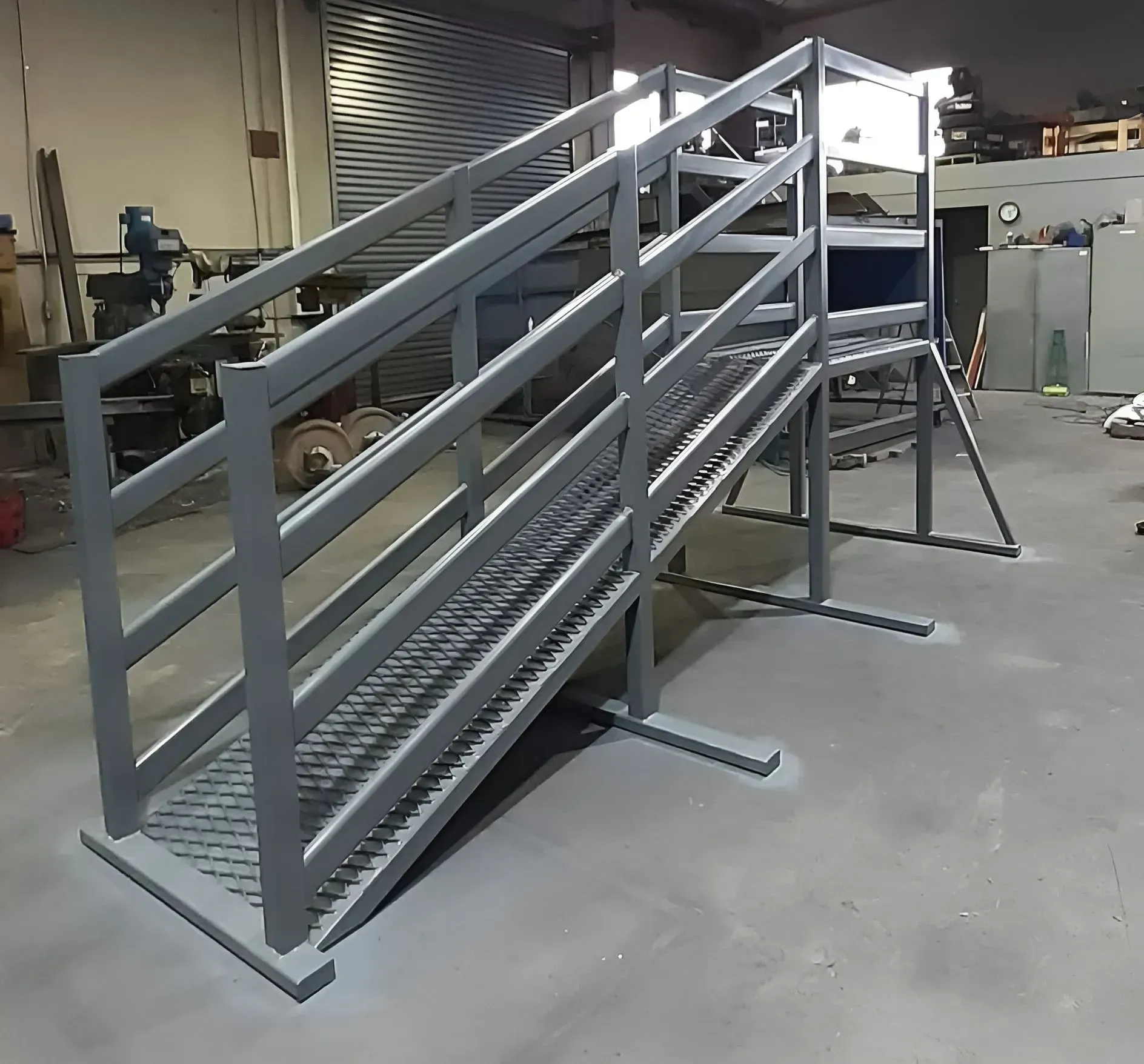 Gray metal industrial ramp with handrails and grated steps in a warehouse-like setting