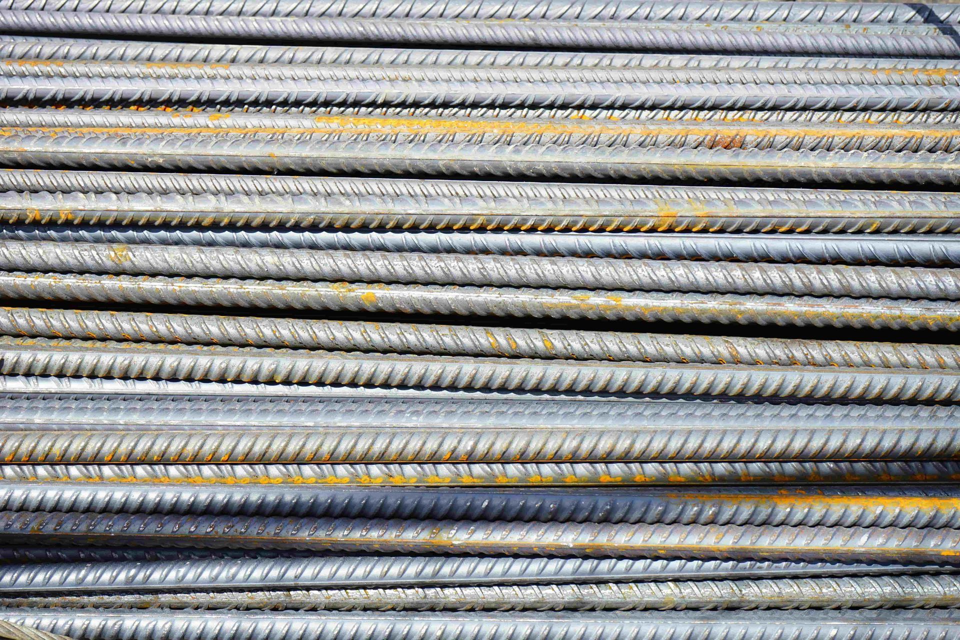 Stacked gray metal rebar rods with yellow paint marks arranged horizontally