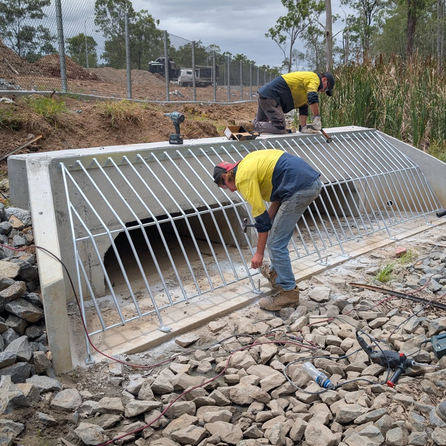 Workers installing a metal grate over a concrete drainage culvert at a rocky construction site
