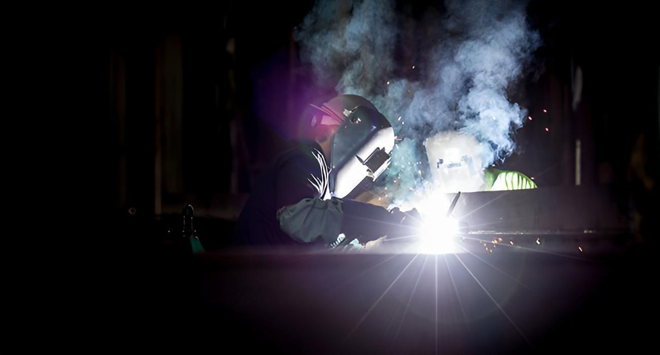 Person welding metal at night, bright sparks and smoke illuminating the dark scene.