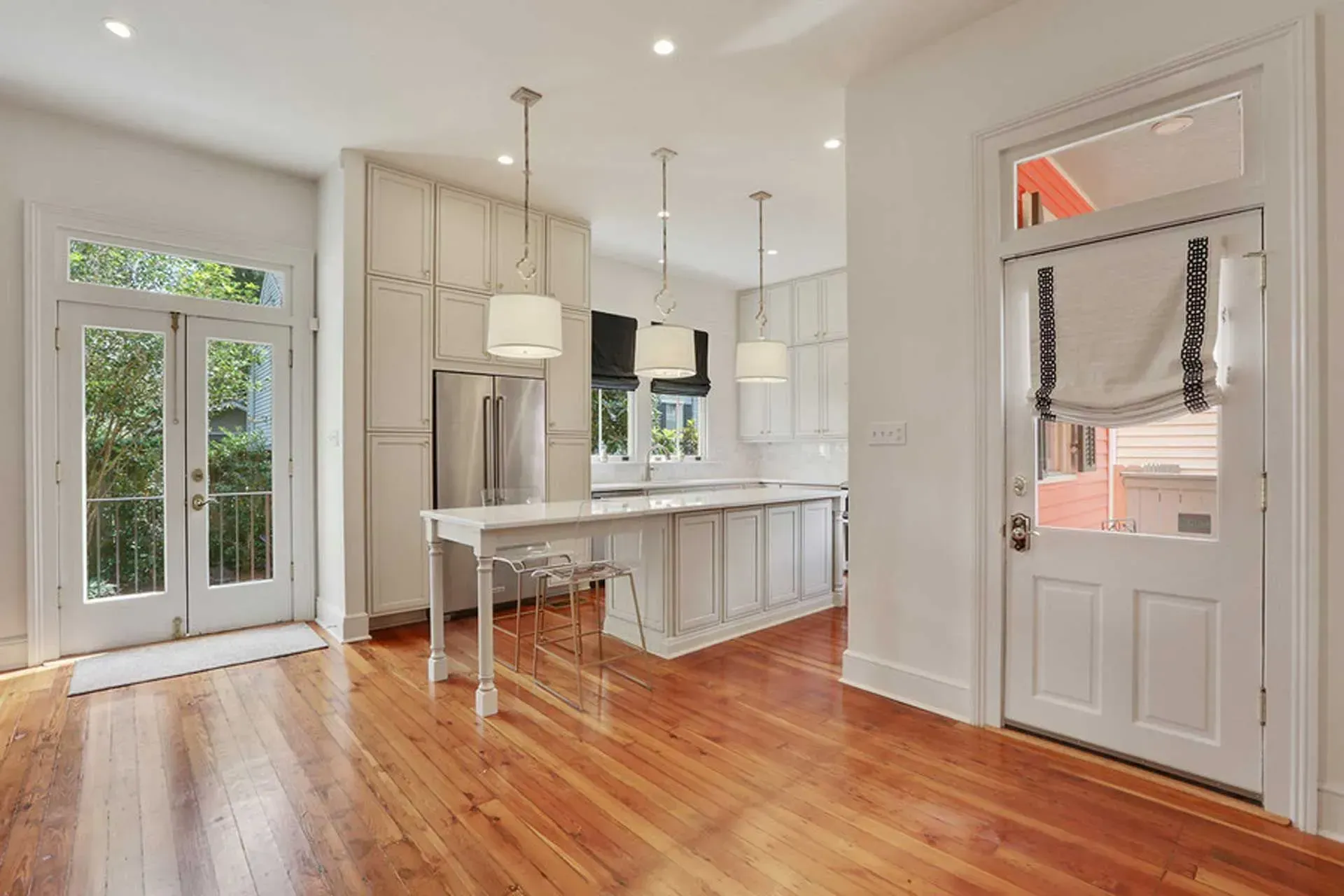 Bright, open kitchen with white cabinets, island, and wood floors. French doors and entry door visible.