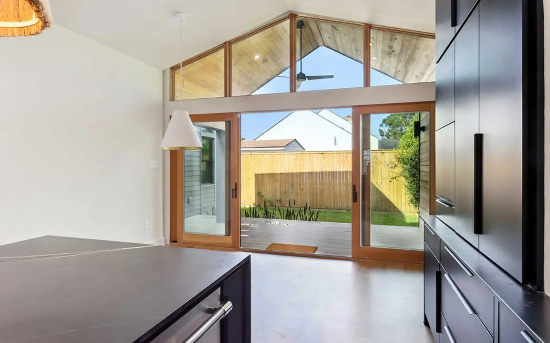 Kitchen with large wood-framed glass doors and window, overlooking a small yard. White walls, black cabinets.
