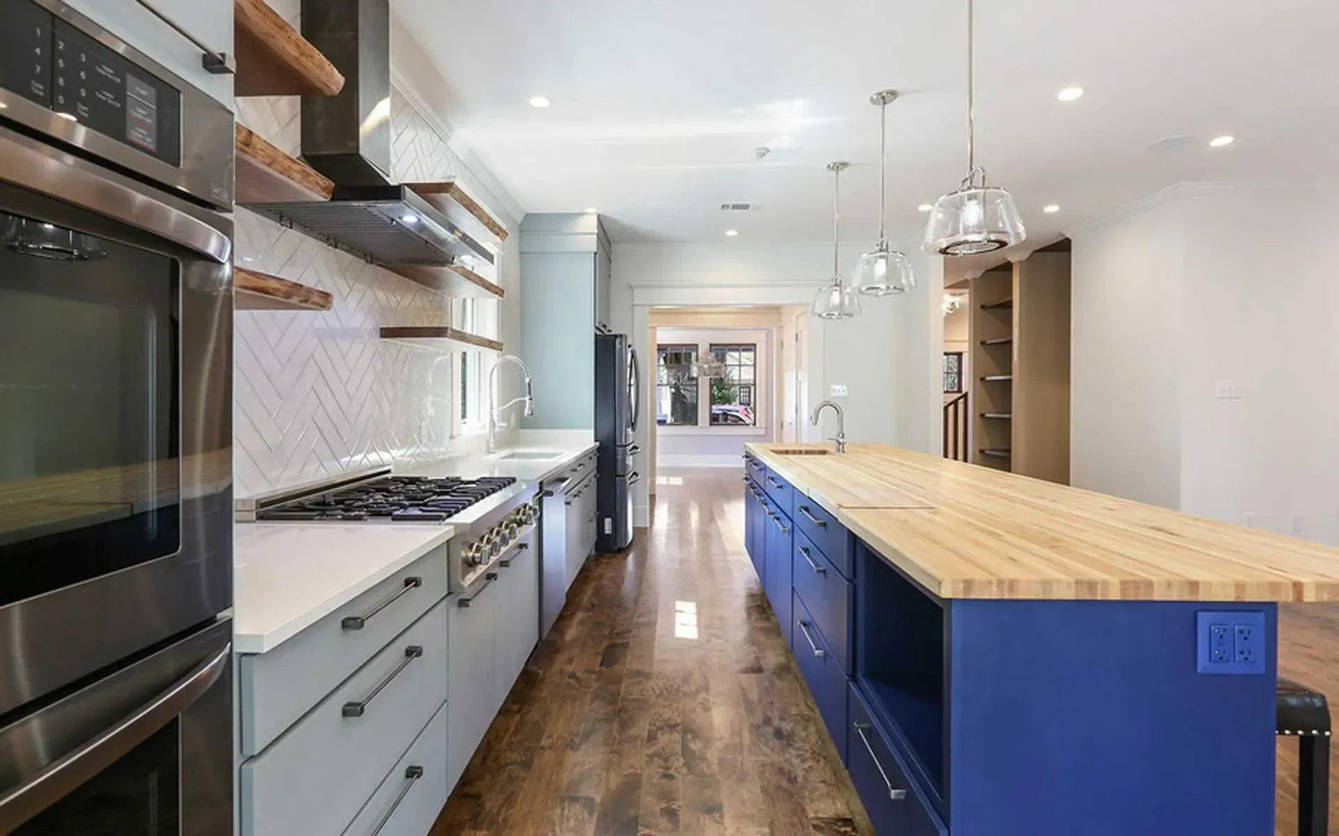 Modern kitchen with blue and gray cabinets, stainless steel appliances, and a butcher-block island.