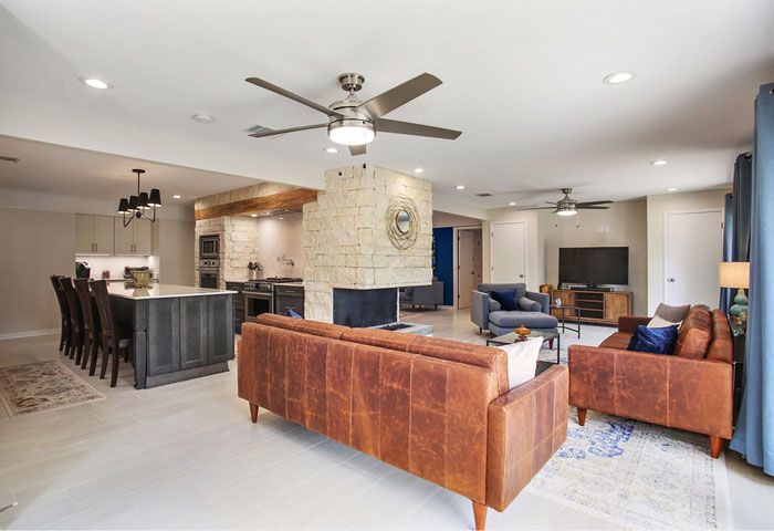 Open-concept living space with a kitchen, living room, and fireplace. Brown leather furniture, light wood floors.