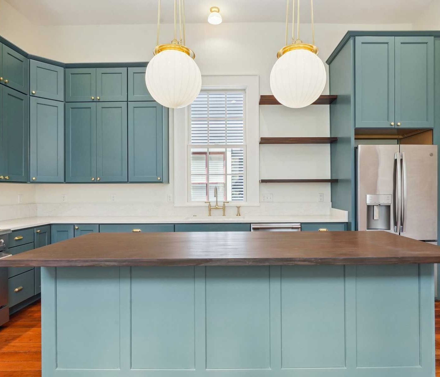 Blue kitchen with island, white countertops, and globe pendant lights.
